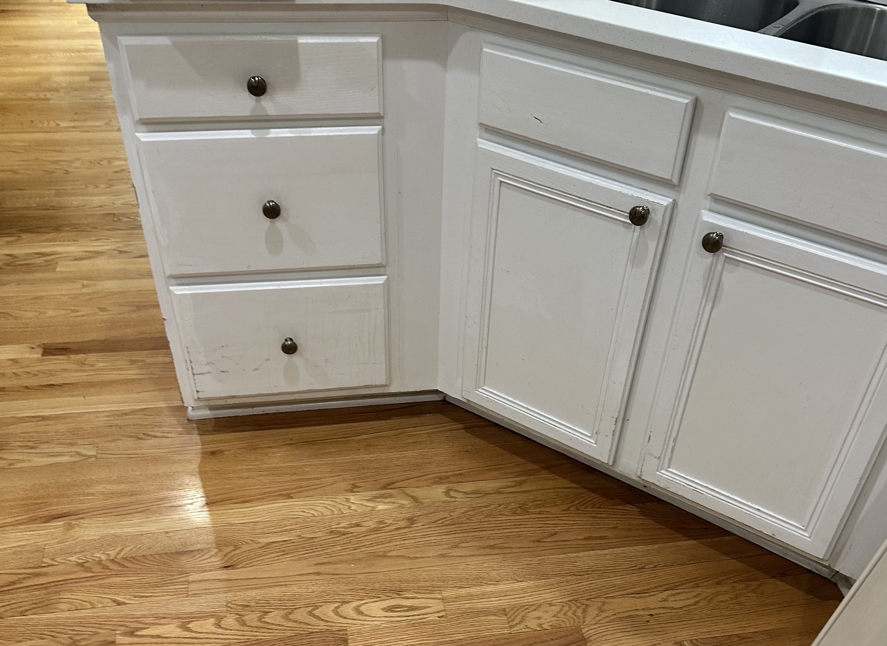 A kitchen with white cabinets and wood floors.